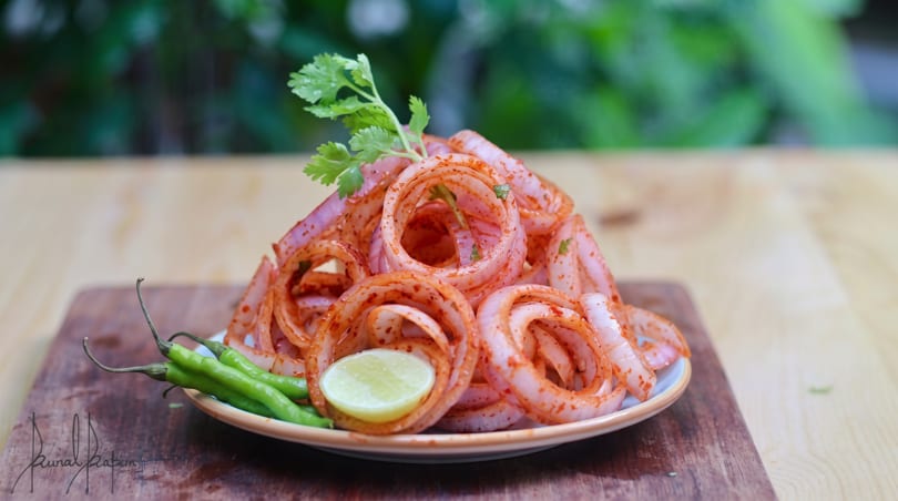 Spicy red onion rings with cilantro, green chilies, and a lime wedge on a plate.