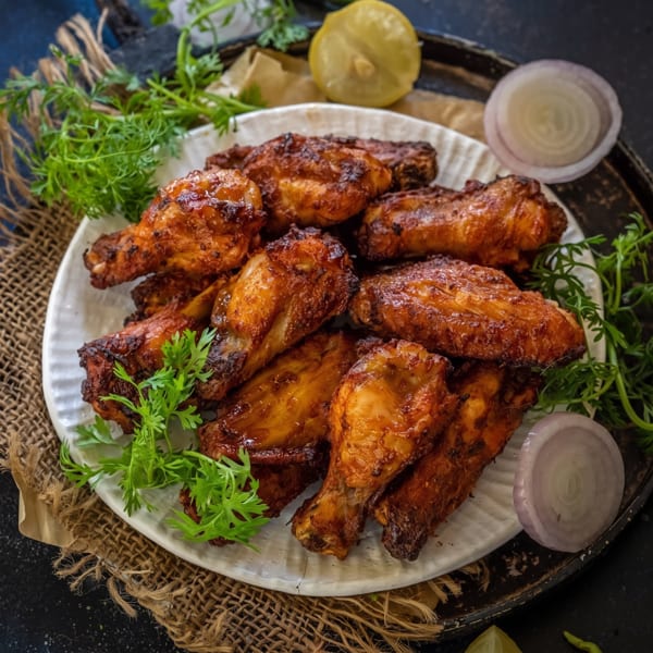 A white plate filled with crispy, glazed chicken wings, garnished with fresh cilantro, lemon, and red onion.