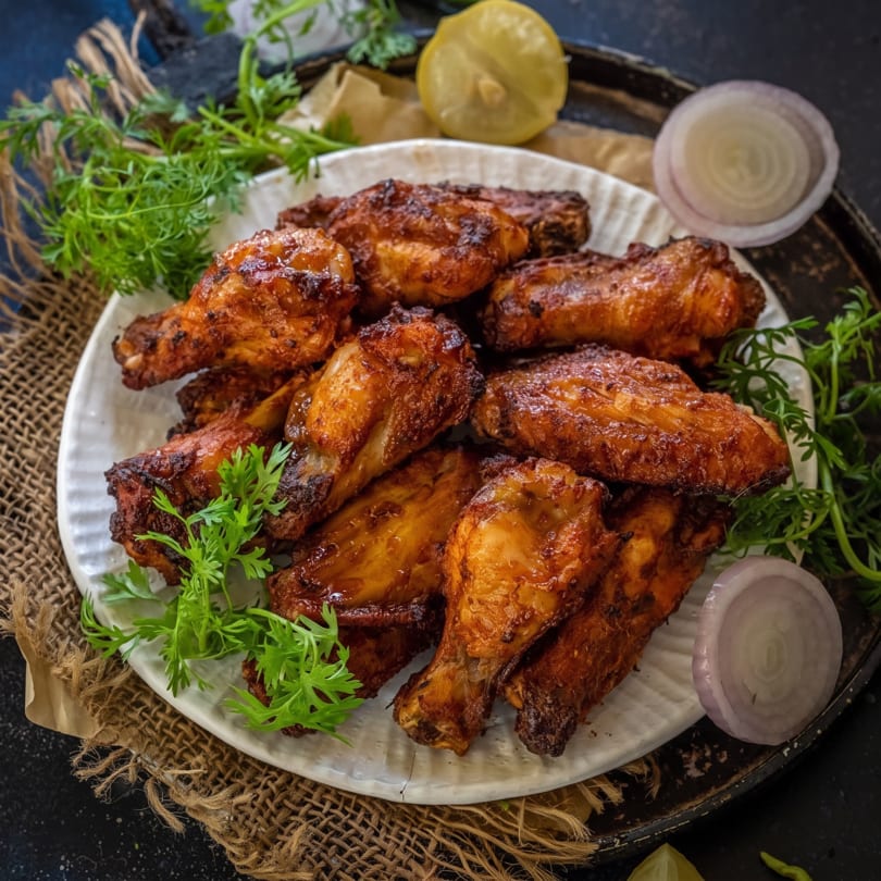 A white plate filled with crispy, glazed chicken wings, garnished with fresh cilantro, lemon, and red onion.
