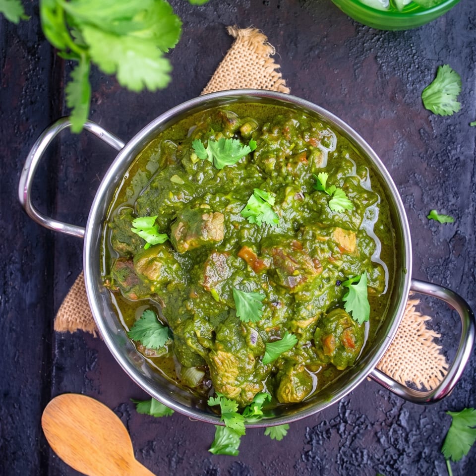 Overhead view of green curry with meat in a metal bowl, garnished with cilantro.