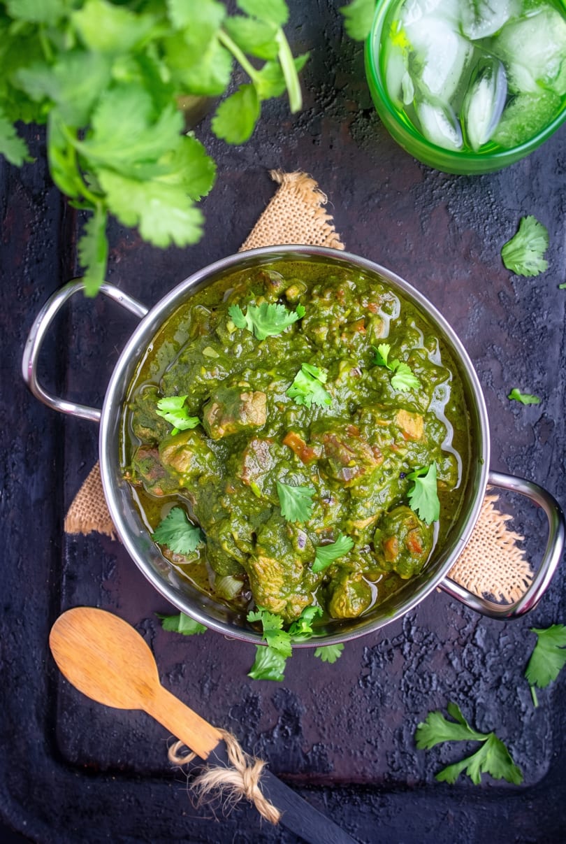 Overhead view of green curry with meat in a metal bowl, garnished with cilantro.