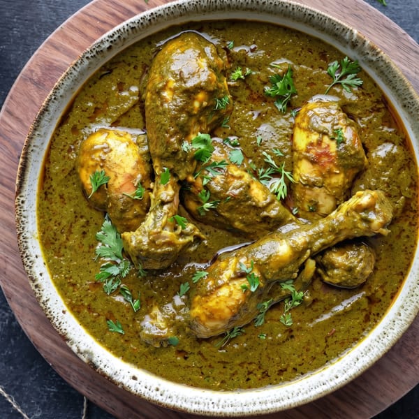 Chicken drumsticks and thighs in a vibrant green curry, garnished with fresh cilantro in a rustic bowl.