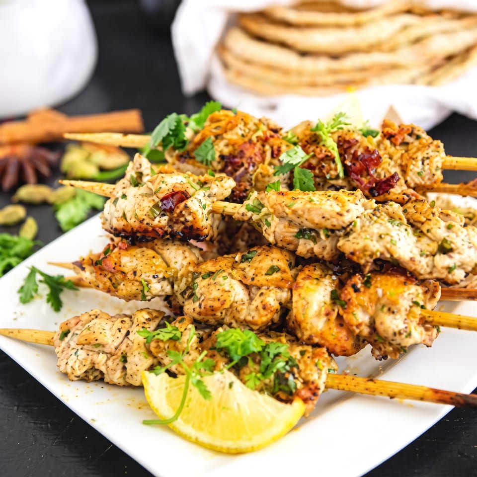 Grilled chicken skewers with fresh herbs and a lemon wedge on a white plate.