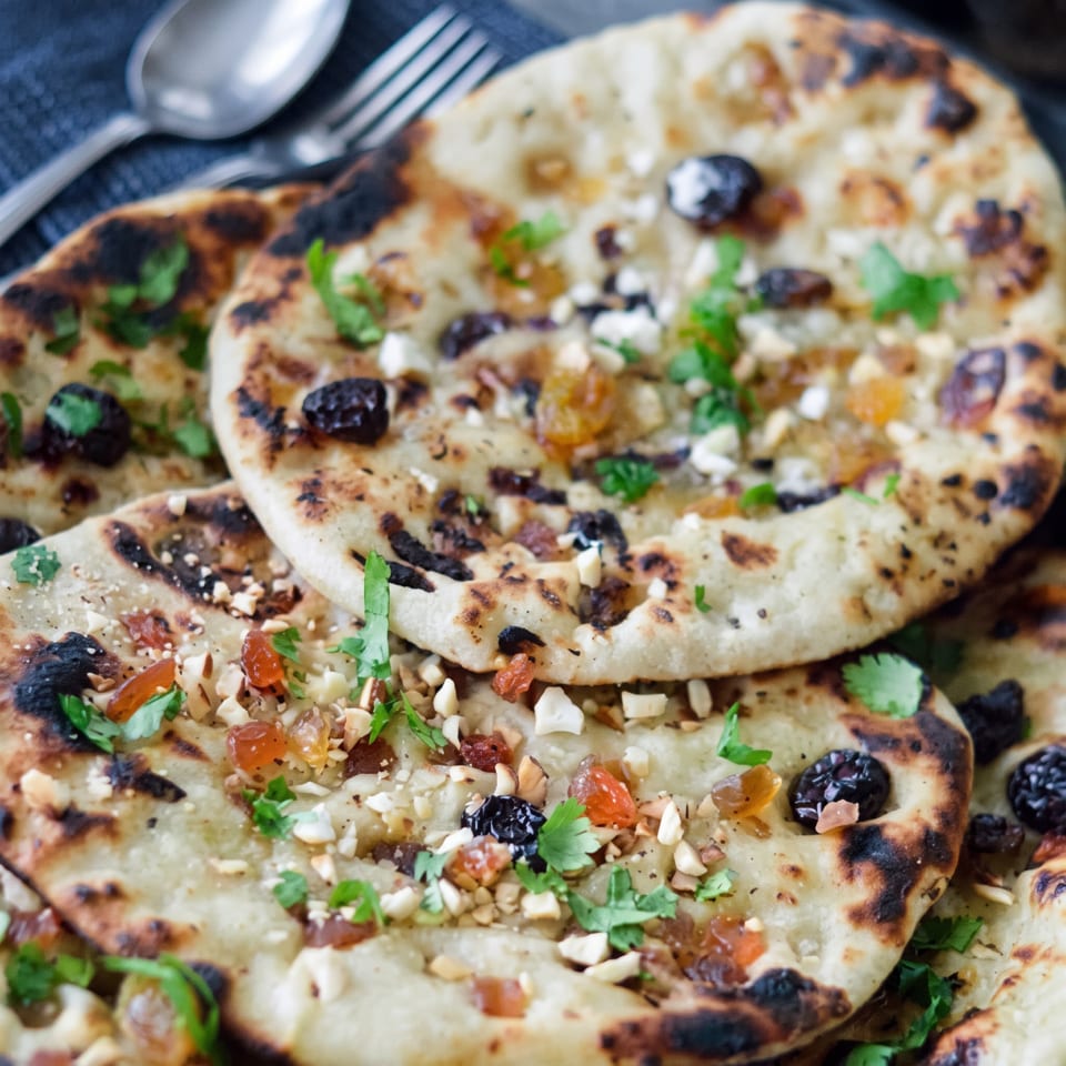 Close-up of golden brown naan bread topped with nuts, raisins, and fresh cilantro.