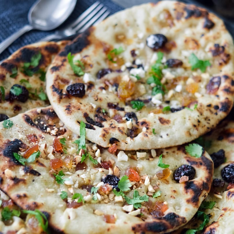 Close-up of golden brown naan bread topped with nuts, raisins, and fresh cilantro.